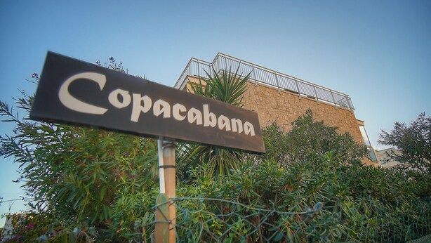 Une enseigne portant le nom « Copacabana » devant un immeuble doté d’un balcon.
