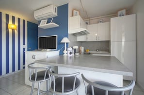 A modern kitchen with a central island, bar stools, white cabinetry, and a blue accent wall. - FRGK - Copacabana Palm Beach Studio (Cannes)