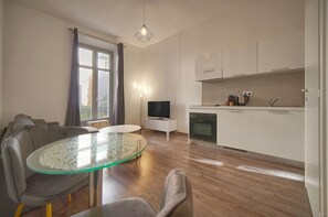 Een moderne keuken met witte kastjes, een ingebouwde oven en een eethoek met een glazen tafel en grijze stoelen.