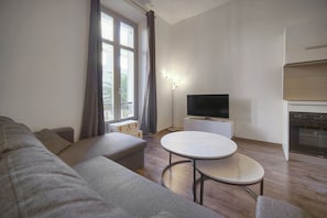 Un salon comprenant un canapé, une petite table ronde, un téléviseur à écran plat et un coin cuisine avec un four.
