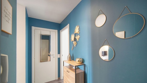 Ein Flur mit blauer Wand, einer Holzkommode und drei an der Wand befestigten Spiegeln.