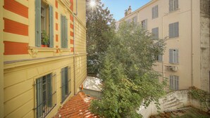 Ein schmaler Gang zwischen Gebäuden mit einem Baum in der Mitte, einer kleinen Bank und einem Ziegeldach.