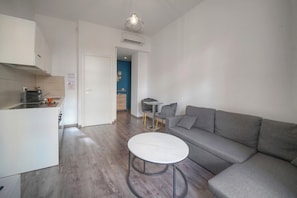 Ein stilvoller Wohnraum mit Küche, einem grauen Sofa, einem runden Couchtisch und einem Essbereich mit kleinem Tisch und Stühlen.