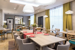 Ein Hotel-Essbereich mit mehreren Tischen, Stühlen und Pendelleuchten.