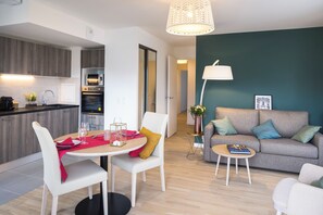 Une cuisine moderne équipée d’appareils électroménagers, un coin repas avec une table et des chaises, et un salon avec un canapé et une lampe.