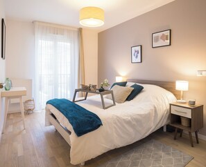 Une chambre bien rangée, avec un lit, une table de chevet, une lampe et un petit bureau avec une chaise.
