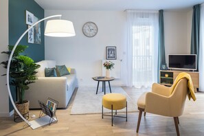Un salon moderne avec un canapé, un fauteuil, une lampe, un téléviseur et une plante en pot.