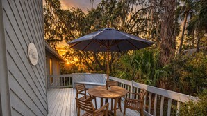 Una terraza de madera con una mesa y sillas, rodeada por una barandilla y un gran paraguas.