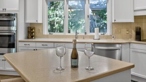 Una cocina con armarios blancos, un horno de acero inoxidable, una botella de vino y dos copas de vino sobre la encimera.