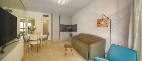 A modern living room with a sofa, a TV, a dining area with chairs, and a kitchen area.