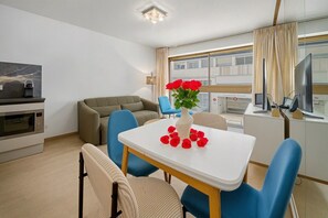 A modern hotel room with a dining area, a sofa, a table with a vase of red flowers, and a kitchen area with a microwave. - One-bedroom apartment in Nice, France (Niza)