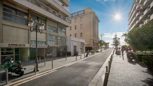 Ein mehrstöckiges Gebäude mit Balkonen, eine Straße mit abgestellten Rollern und ein klarer Himmel.