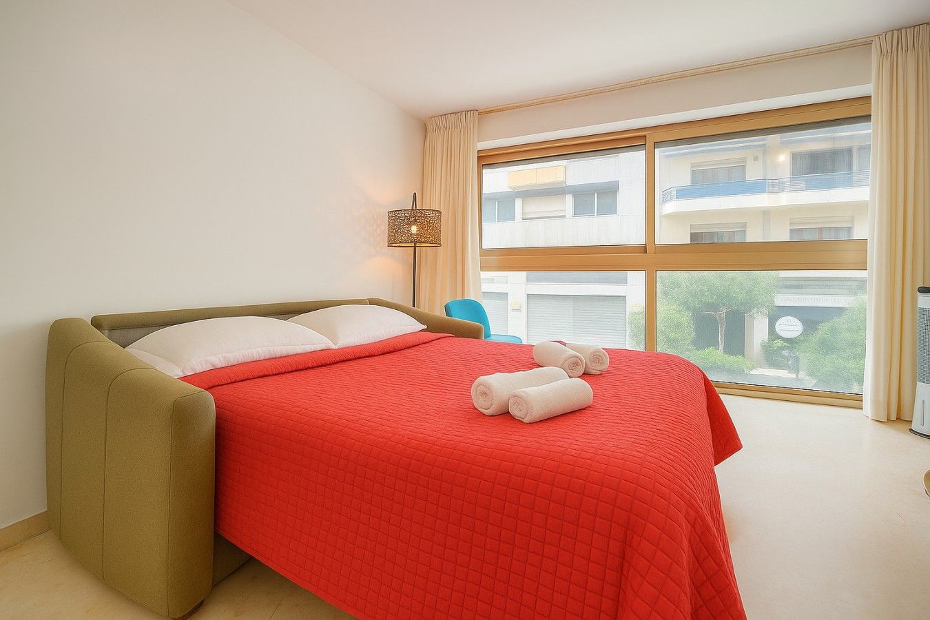 A hotel room with a bed, a window, and a view of a building outside.