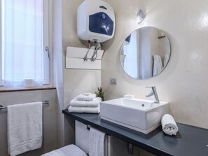 Um banheiro com pia branca, espelho, porta-toalhas e janela com cortinas.