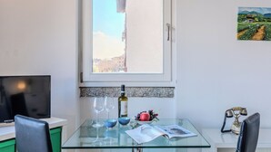 Ein Zimmer mit Glastisch, zwei Weingläsern, einer Weinflasche, Obstschale, Zeitschrift, Telefon und Fernseher.