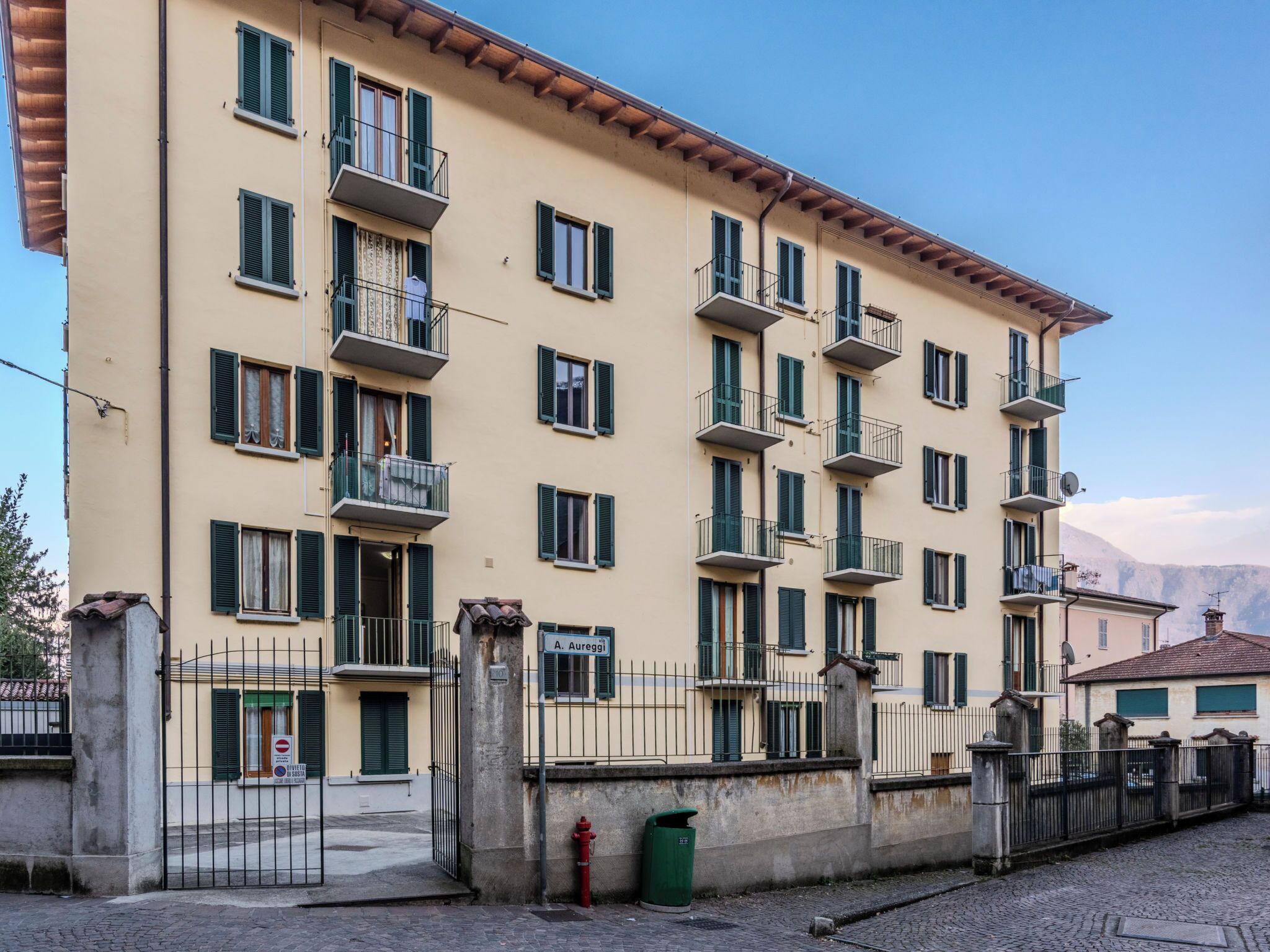 A multi-story building with balconies, a gated entrance, and a cobblestone street.
