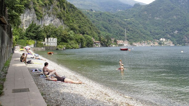 A lakeside beach with people sunbathing and swimming, surrounded by mountains and a small town. - Casa Luvit by Interhome (Menaggio)