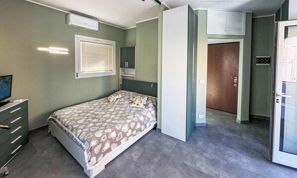 Une chambre à coucher comprenant un lit, une commode, une fenêtre avec des stores, une porte et un climatiseur fixé au mur.