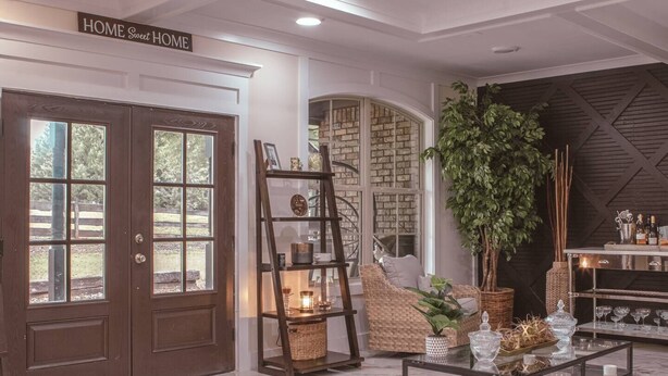 Un salón luminoso con una puerta grande de madera, un sofá de mimbre, una mesa de centro de vidrio y una estantería.