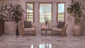 Una habitación con dos sillones de mimbre, una mesita con una vela y un jarrón grande con flores.