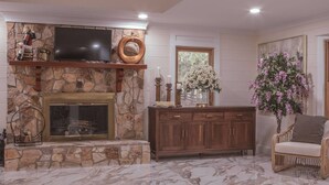 Una sala de estar con chimenea de piedra, un televisor montado encima, un mueble de madera y un sillón de mimbre.