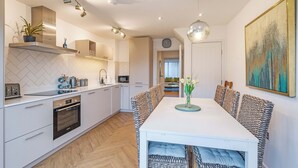 A modern kitchen with white cabinetry, a dining area with patterned chairs, and a large abstract painting on the wall. - HH 120m2 | Fast wi-fi | Work | Holiday |BBQ | Pet (Tonbridge)