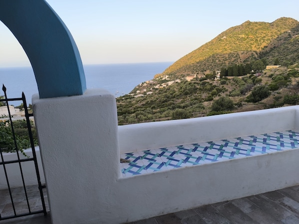 A balcony with a tiled floor, a blue arch, and a view of a coastal landscape with buildings and hills.