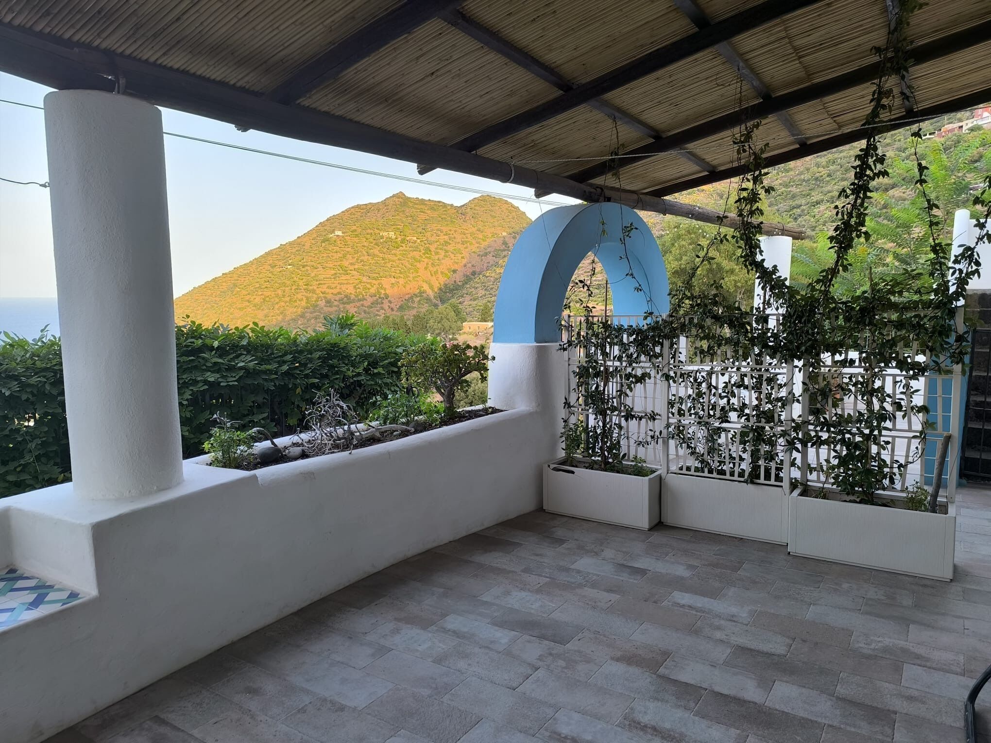 Un espacio al aire libre cubierto con vistas a la montaña, paredes blancas y una estructura en arco azul.