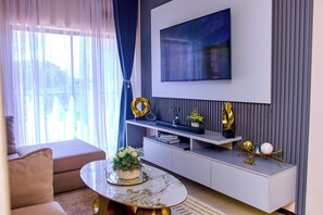 A modern living room with a sofa, a coffee table with flowers, a TV mounted on the wall, and a decorative shelf.
