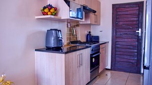 A modern kitchen with light wood cabinets, a gas stove, a coffee maker, and a fruit bowl on a shelf. - The perfect 2-bedroom apartment Designed for those who value neatness. (Harare)