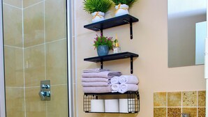 A bathroom with a shower, toilet, sink, and shelves with towels and plants. - The perfect 2-bedroom apartment Designed for those who value neatness. (Harare)