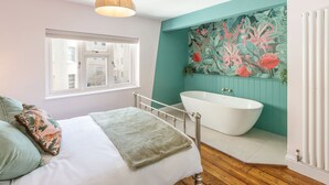 Een slaapkamer met een bed, een raam, een witte badkuip en een bloemen behang.
