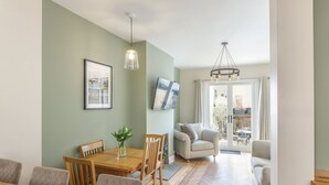 Een eetgedeelte met een houten tafel en stoelen, een vaas met een plant en een lijst met een afbeelding aan de muur.