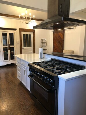 A kitchen with a central island, a stove, oven, and a chandelier. - Historic Belle Maison: Billiards Room, Fire Pit & Magnolia Charm (Magnolia)