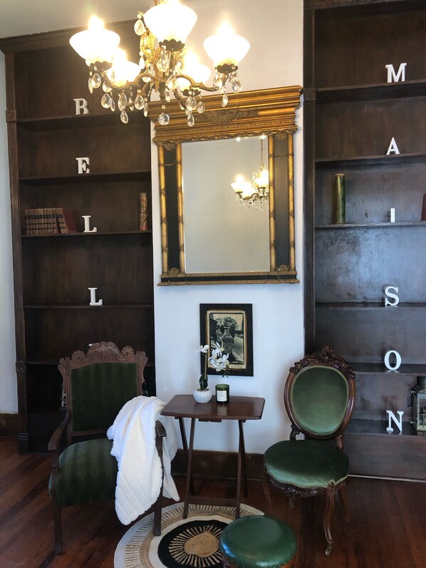 A room with a large mirror, a chandelier, a small table with a vase, two chairs, and a bookshelf with letters. - Historic Belle Maison: Billiards Room, Fire Pit & Magnolia Charm (Magnolia)