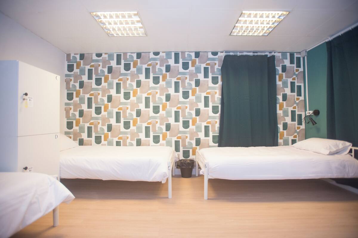 A room with two single beds, a patterned wall, a trash bin, and a door.