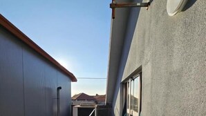 A narrow corridor with a metal railing, a window, and a door on the right, leading to a balcony with a view of the sky and distant mountains. - Aerostay Hostel (Maia)