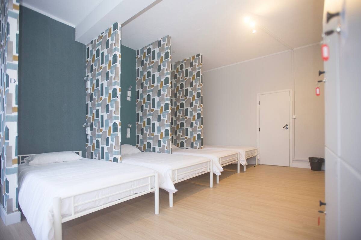 A room with three beds, a white door, and a patterned wall.