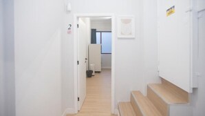 A hallway with a staircase leading to a room, a door with a number, and a window in the background. - Aerostay Hostel (Maia)