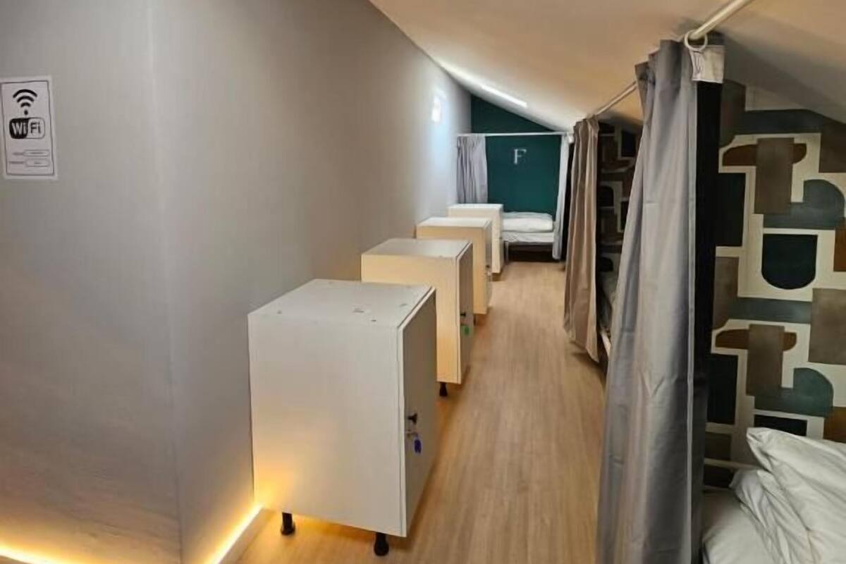 A modern, compact room with a sloped ceiling, a bed, a desk, and a small seating area.