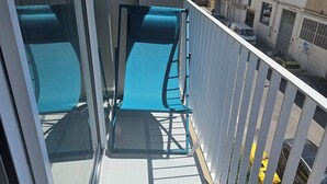 A balcony with two blue chairs, a small table, and a view of parked cars and buildings. - Air-conditioned apartment with balcony, wifi, near ramparts (Avignon)