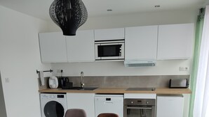 A modern kitchen with white cabinets, a microwave, a toaster, and a dishwasher. There is a wooden dining table with two chairs. - Air-conditioned apartment with balcony, wifi, near ramparts (Avignon)