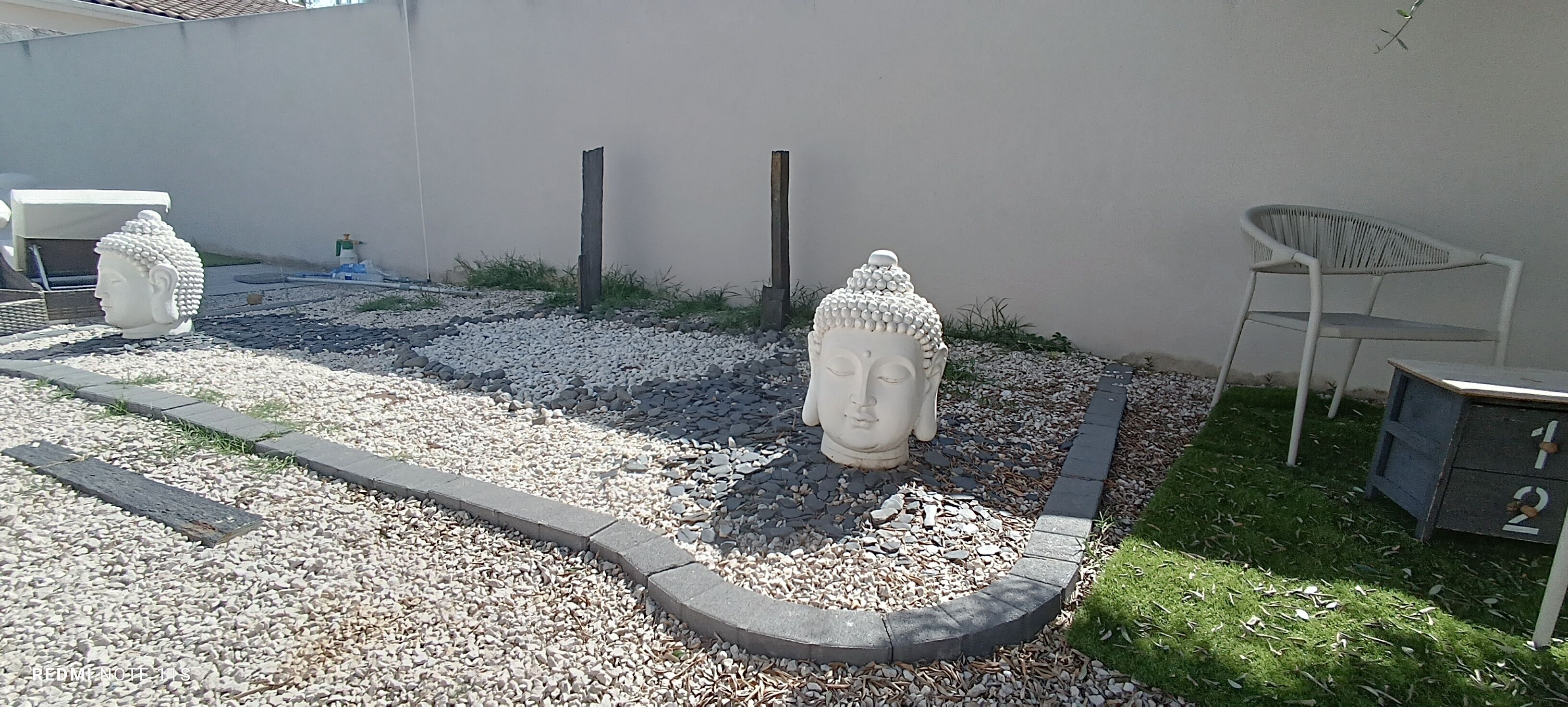 A garden with a Buddha statue, a white chair, and a small table.