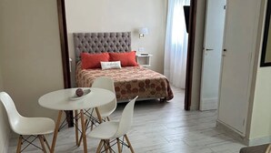 Une chambre à coucher comprenant un lit, une table de chevet, une lampe, une table à manger avec des chaises et une porte.