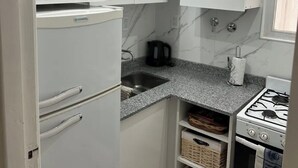 Une cuisine compacte équipée d’un four à micro-ondes encastré, d’un évier, d’une cuisinière à gaz et de meubles de rangement blancs.