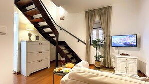 Un salon avec un canapé, une table à manger dressée, un téléviseur, un escalier et une plante.