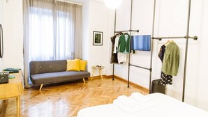 Ein Zimmer mit einer Couch, einem Bett, einem Kleiderständer und einem kleinen Tisch.