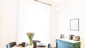Ein Essbereich mit einem Tisch für zwei Personen, einer Blumenvase, einer blauen Kommode mit Schubladen und einem gerahmten Bild an der Wand.