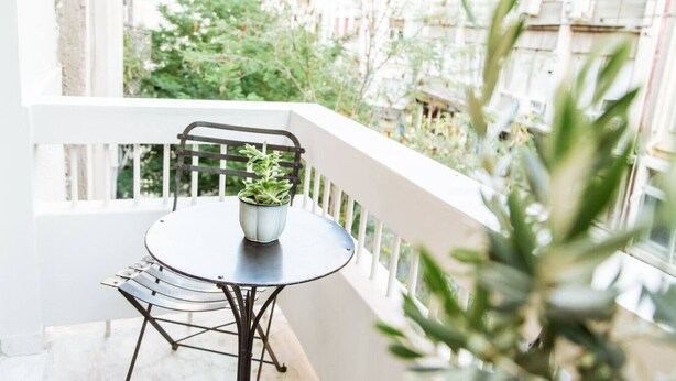 Ein Balkon mit Tisch und Topfpflanze, umgeben von Grünflächen und Gebäuden.