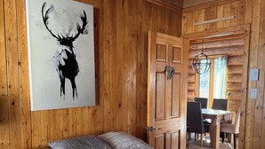En stuga med träpanel på insidan, innehållande en säng, en målning av ett rådjur och en matplats.